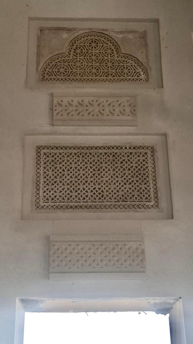 An installed gypsum composition: arched panel, bands and a pierced rectangular panel on a plaster wall